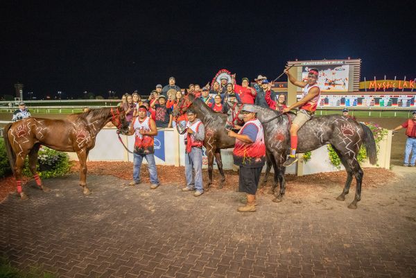 Team in red shirts presenting horses in Winner's Circle.